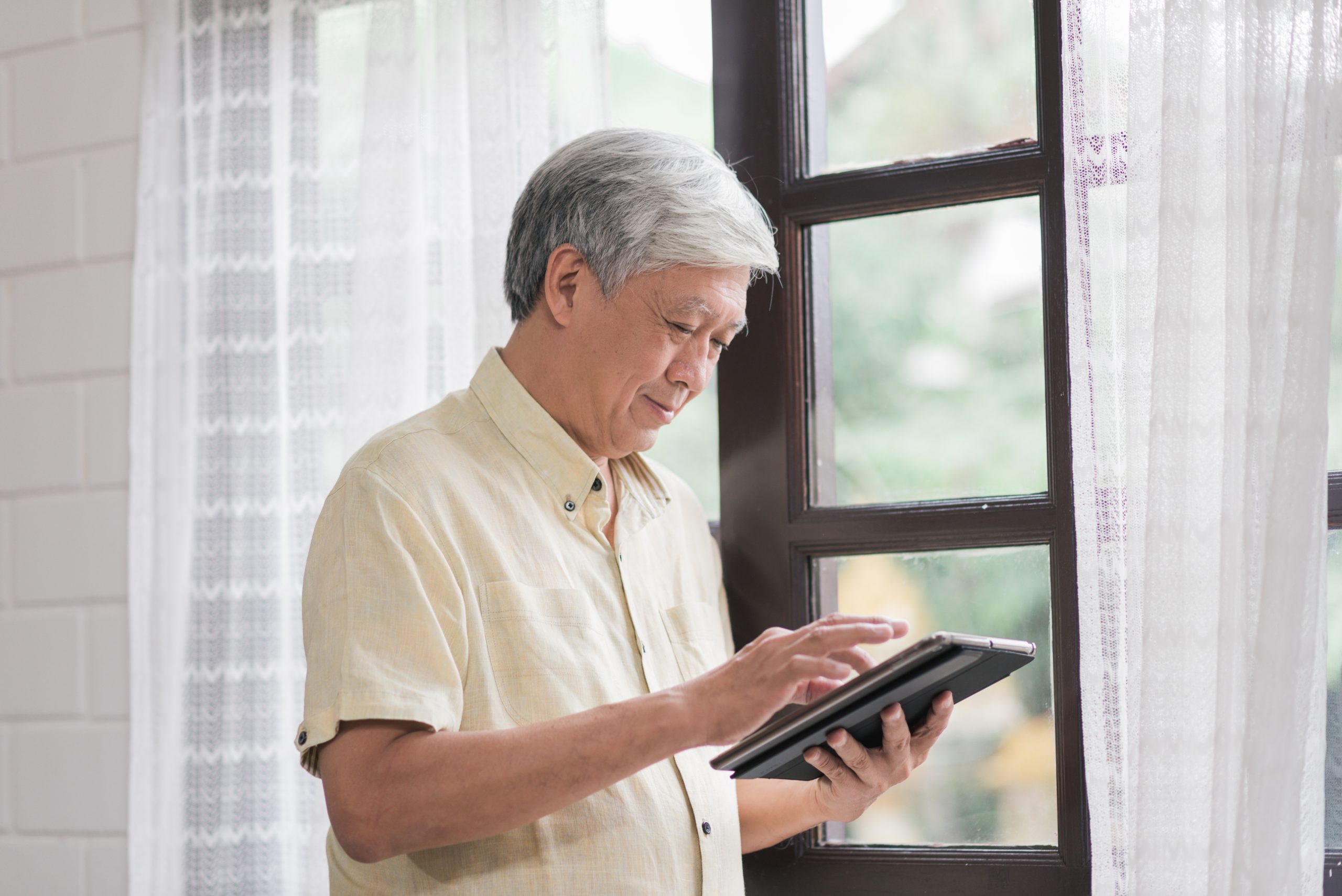 asian elderly man using tablet checking social media near window